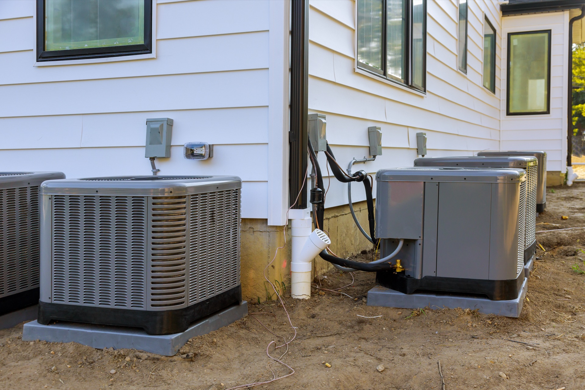 Multiple HVAC units installed outside residential homes with white siding and foundation pads